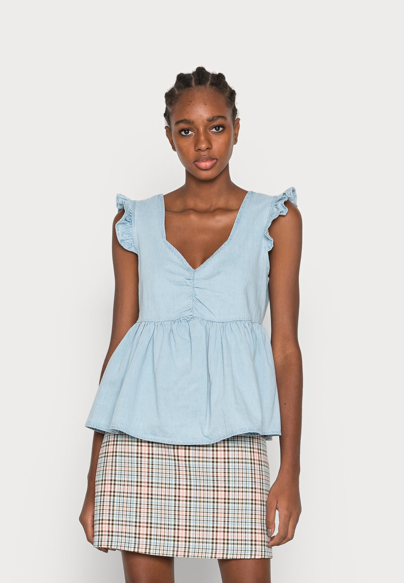 Top de chambray azul claro com decote em V e mangas com volantes, combinado com uma saia xadrez estampada em tons bege, azul e castanho.