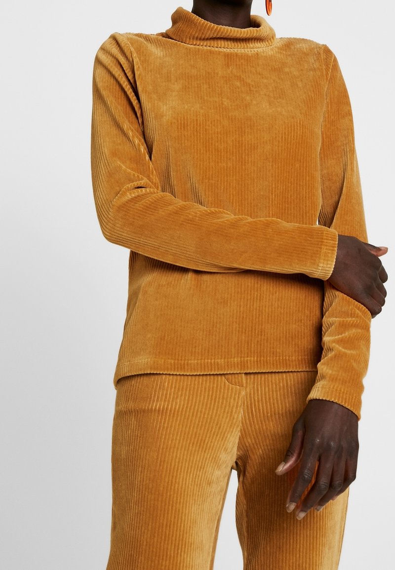 Senfgelbe Cordkleid mit Rollkragen und langen Ärmeln, das eine gerippte Textur aufweist. Der Stoff erscheint weich und leicht glänzend.