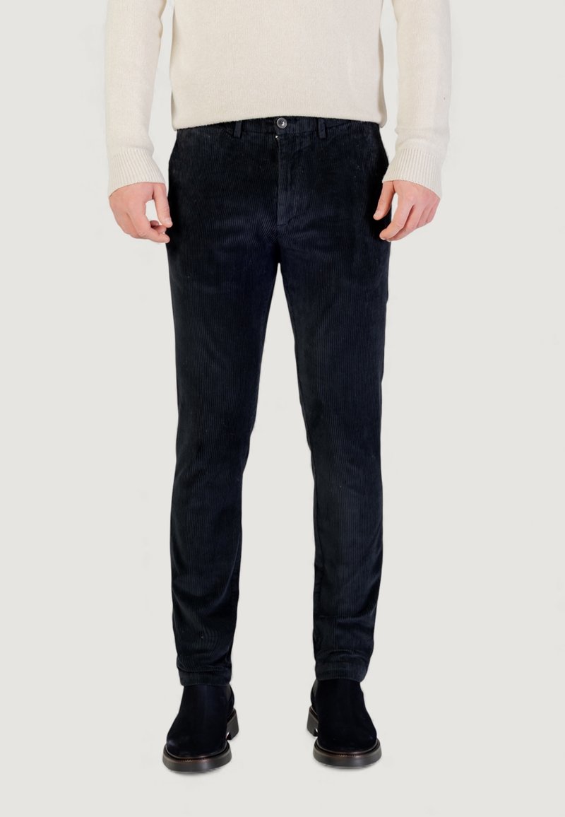 Pantaloni in velluto a coste blu scuro con una texture a coste, dotati di chiusura con bottoni, tasche frontali e design slim fit. Abbinati a stivali alla caviglia neri.