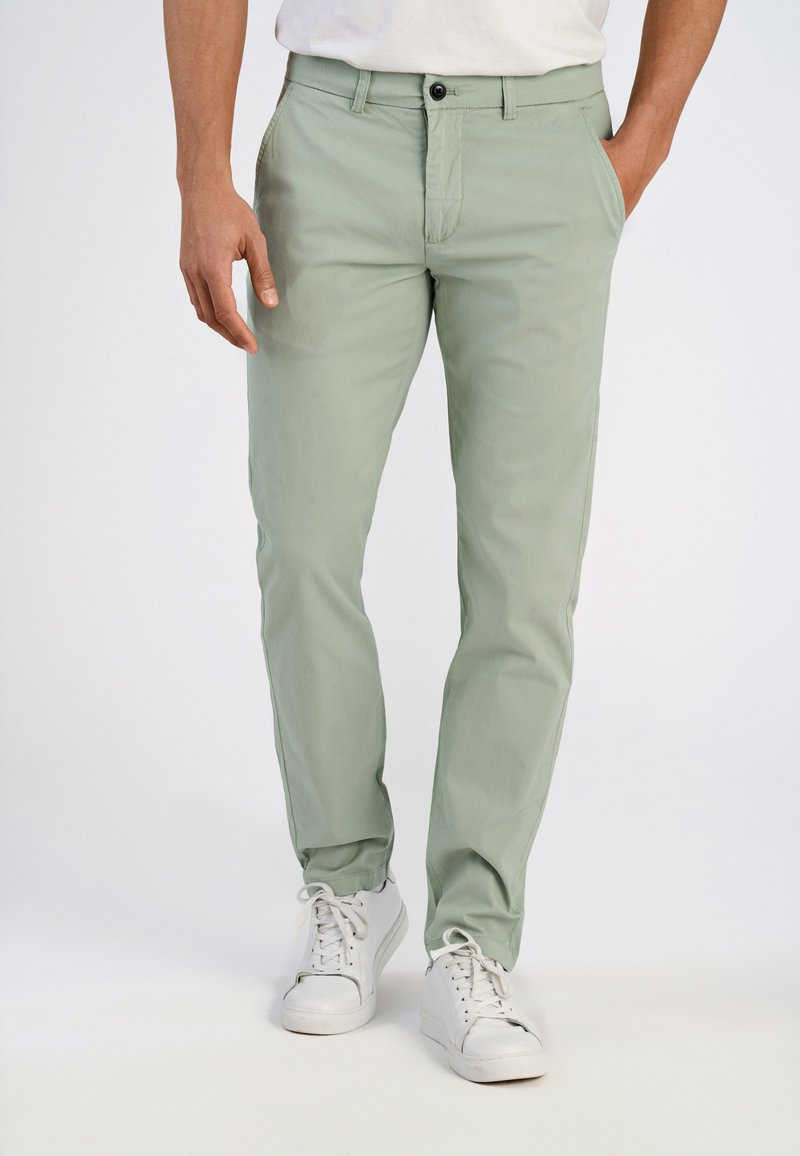 Chinos vert clair en tissu coton mélangé, avec une coupe droite, des poches frontales et une fermeture à un seul bouton. Assortis à des baskets blanches.