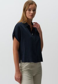 Camicia a maniche corte blu navy realizzata in tessuto testurizzato. Presenta un colletto e una chiusura davanti con bottoni, con una vestibilità comoda e fessure laterali.