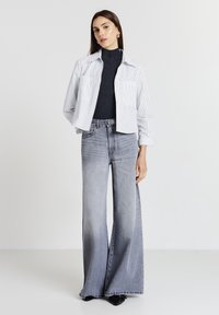 Chemise cropped rayée en blanc et bleu, associée à un jean large gris. Un col roulé en tricot texturé en dessous. Des chaussures noires complètent la tenue.