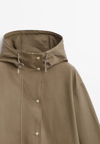 Brown hooded jacket with a relaxed fit, snap buttons, drawstring hood, and smooth fabric texture. Features minimalist design details.