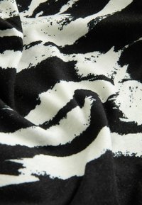 Svart och vit tyg med ett djärvt, abstrakt mönster med böjda linjer och penseldrag. Mjuk bomullstextur, något skrynklig.