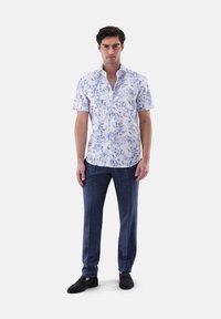 Kurzärmliges weißes Hemd mit blauem Blumenmuster, mit Knopfdown-Kragen, kombiniert mit dunkelblauen strukturierten Hosen und schwarzen Slippers.