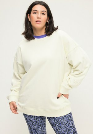 Světlý krémový oversized svetr s žebrovanou texturou a volnými rameny, doplněný o modré legíny s leopardím vzorem. Bílé logo na rukávu.