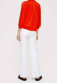 Czerwony sweter typu pulower z rękawami do łokcia, w połączeniu z białymi dzwonowatymi jeansami. Jeansy mają tylne kieszenie i gładką fakturę.