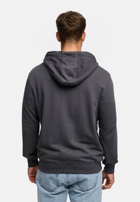 Donkergrijze hoodie met een grote capuchon, geribde mouwen en zoom. Getextureerde stof met een gladde afwerking. Gecombineerd met lichtblauwe spijkerbroek.