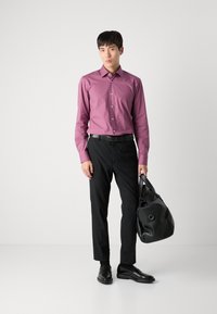 Férfi hosszúujjú, gombos ing mauve színben, fekete nadrággal és cipővel párosítva. Egy ívelt tetejű, fogantyús fekete bőrtáskát tart.