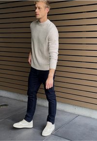 Vaalea harmaa neulepaita, tummat farkut ja beiget tennarit. Neulepaidassa on ribbireunukset kauluksessa ja hihoissa; farkut ovat istuvat. Neutraalit sävyt luovat rentoa ilmettä.