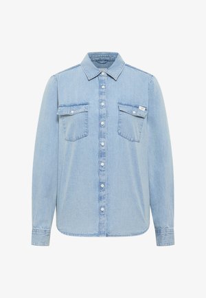 Chemise en denim bleu clair à manches longues avec col pointu et deux poches poitrine à rabat, dont une avec une petite étiquette blanche.