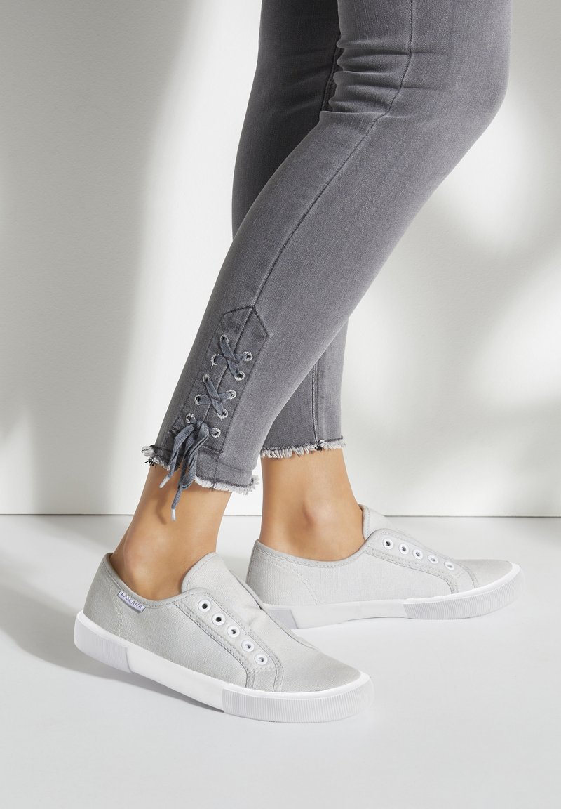 Graue Leinenschlüpfsneaker mit weißen Gummisohlen und Metallösen. Getragen mit grauen Skinny-Jeans, die eine Schnürdetail am Knöchel zeigen.