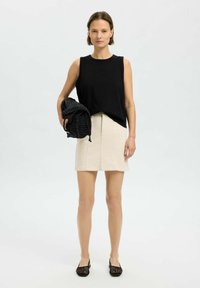 Must have sleeveless must liigenditops, beež seelik tekstuuriga viimistlusega, musta võrkkoti hoidmine ja jalas mustad avatud varbaga kingad.