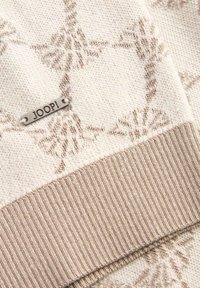 Jersey de punto con un patrón beige texturizado, dobladillo acanalado y una etiqueta plateada de JOOP! adjunta. Los materiales son suaves y cálidos.