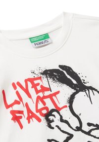 Camiseta blanca con texto en graffiti rojo "LIVE FAST" y una ilustración abstracta negra de Snoopy de Peanuts cerca de la etiqueta del cuello.