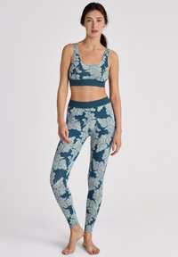 Teal sport-beha en bijpassende leggings met een wit bloemenpatroon. Het materiaal lijkt rekbaar; fitted ontwerp met brede elastische banden.