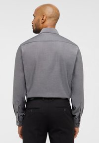 Grau langärmliges Shirt mit feiner Textur, geknöpften Manschetten und Kragen, kombiniert mit schwarzen Hosen mit Gesäßtaschen.