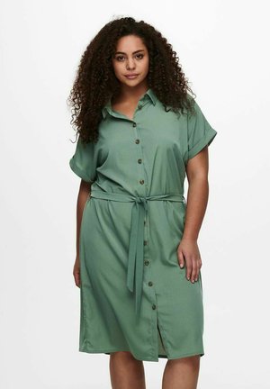 Sage green shirt dress with a button-down front, short rolled sleeves, and a matching fabric tie at the waist. Soft texture, knee-length.