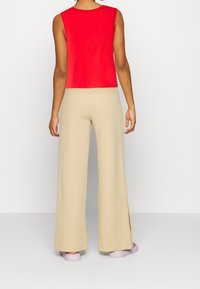 Haut rouge sans manches associé à un pantalon beige ample et léger, avec des fentes latérales et des chaussures slip-on violettes. Design simple et décontracté.