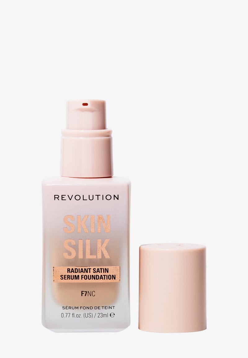 Fond de teint sérum Revolution Skin Silk dans un flacon en verre givré avec un distributeur rose. L'étiquette présente des lettres dorées indiquant la teinte F7NC.