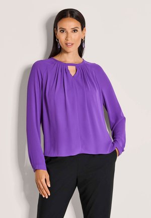 Lila Bluse mit langen Ärmeln, einem ausgeschnittenen Ausschnitt, gefältelter Vorderseite und geknöpften Manschetten, kombiniert mit schwarzen Hosen für einen Kontrast.