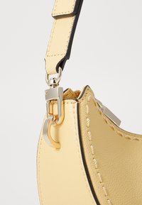Sac en cuir jaune avec des bordures noires contrastantes, comportant un fermoir en métal et des détails de couture visibles sur le bord.