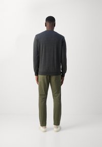 Pull gris foncé avec un col rond, associé à un pantalon vert olive et des baskets blanches. Texture lisse, coupe décontractée, style casual.