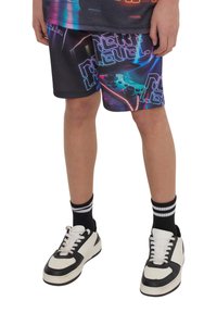 Pantaloni corti grafici neri e colorati con design videoludico; contrastano con delle sneaker bianche e nere e calzini a righe nere.