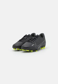 Botas de fútbol Nike Mercurial negras con tachuelas amarillas neón y cordones negros sobre un fondo blanco, inclinadas ligeramente a la derecha.