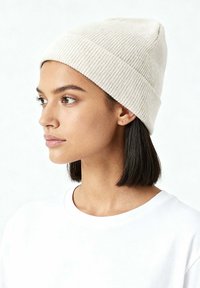 Crèmekleurige gebreide beanie met een geribbelde structuur, taps toelopend tot een punt aan de bovenkant. Combinatie met een wit overhemd, met een gladde stof.