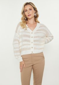 Cardigan a righe beige e bianche con scollo a V, maniche lunghe e sei bottoni frontali. Tessuto a maglia morbida, vestibilità casual.