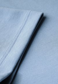 Zacht blauw stof gevouwen, waarbij de fijne textuur en stiksels goed zichtbaar zijn. De afbeelding benadrukt de gladde kwaliteit en kleur van de textiel.