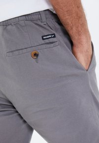 Gray pants with an elastic waistband, side pockets, a back pocket with a brown button, and a black label reading "THREADBARE."