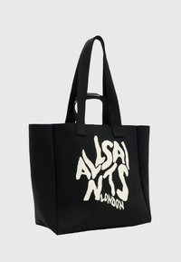 Sac fourre-tout noir avec poignées doubles et texte abstrait blanc qui indique "ALSAINTS LONDON" sur le devant, sur un fond uni.