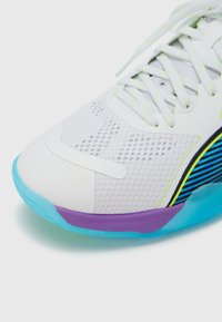 Weißer Sportschuh mit Mesh-Obermaterial, neongelben Akzenten und einer türkisfarbenen Sohle. Lila Detail in der Nähe der Ferse mit einem horizontal gestreiften Muster.