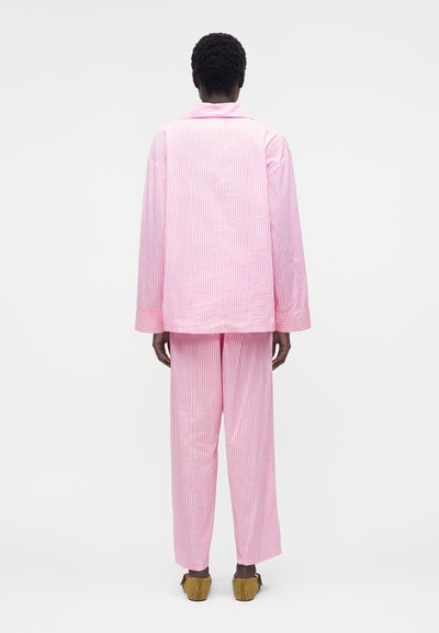 Άτομο φαίνεται από πίσω με φαρδύ ροζ και λευκό ριγέ μακρυμάνικο τοπ και ταιριαστό φαρδύ παντελόνι, με καφέ πλεκτά παπούτσια.