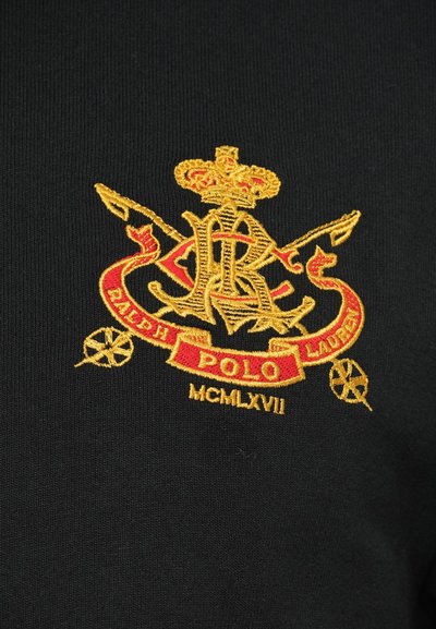 Čierna tkanina má vyšívaný zlatý a červený erb s nápisom "Polo Ralph Lauren" a "MCMLXVII", doplnený o korunu a prekrížené predmety.
