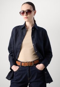 Marine linnen shirt met knoopsluiting, tan getailleerd top, donkere denim jeans en een bruine riem met dubbele gesp, gecombineerd met oversized zonnebril.