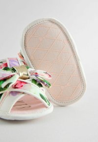 Kukkakuvioiset sandaalit valkoisilla kangasremmeillä, kultaisella yksityiskohdalla ja teksturoidulla vaaleanpunaisella pohjalla, jossa on nauhasuunnittelu.