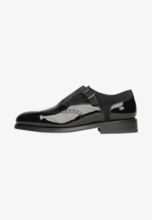 Chaussure habillée pour homme en cuir noir et daim avec boucle à bride de moine et détails brogues, présentée de profil sur fond blanc.