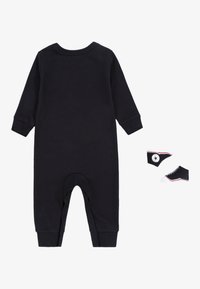 Svart bomullsoverall med långa ärmar och ankelmanschetter, i kombination med svarta och vita babysneakers med en logotyp och röda detaljer.