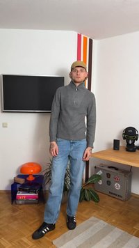 Siv ribasta pletena pulover s polovičnim zadrgo in V-oblikovanim ovratnikom, v kombinaciji s svetlo modrimi naravnost krojenimi jeans hlačami in črnimi teniskami z belimi črtami.