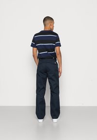 Navy blue-striped t-shirt with short sleeves, paired with dark blue trousers. Smooth fabric and relaxed fit. White sneakers visible.