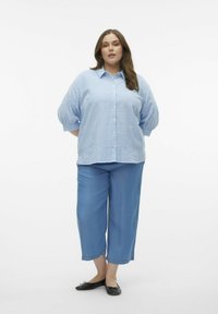 Modrá a bílá pruhovaná oversized košile, s knoflíkovou přední částí, spárovaná s světle modrými zkrácenými kalhotami a černými balerínami. Jednoduchý a ležérní design.