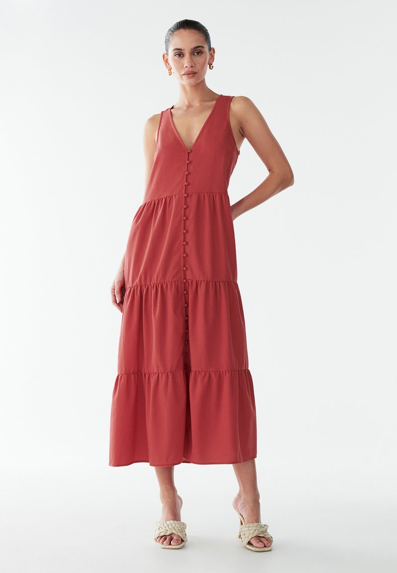 Punane maxi-kleit sügava V-kaelusega, sammastatud disainiga ja nööpidega esiküljel. Valmistatud kerge kangaga, õhukeste rihmade ja lõdva istuvusega.
