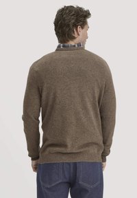 Brauner Wollpullover mit ribbeligem Saum und Bündchen, getragen über einem blau-weiß karierten Hemd, von hinten gesehen. Strukturiertes Strickfinish.