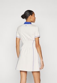 White polo dress with a fitted waist, short sleeves, blue collar, and purple stitching accents. Smooth fabric with a relaxed shape.