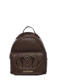 Mochila de cuero marrón con forma redondeada, que cuenta con un bolsillo frontal con un diseño de logo en tono dorado y acentos texturizados.