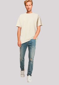 Beige oversized t-shirt, distressed light blue jeans, and white sneakers. The t-shirt has a loose fit and round neckline.