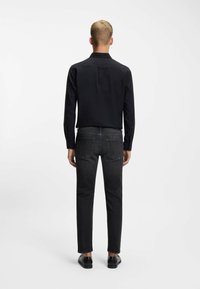 Czarna koszula z długim rękawem w połączeniu z ciemnoszarymi dżinsami. Koszula posiada kołnierzyk oraz standardowy tył. Stopy w czarnych butach.